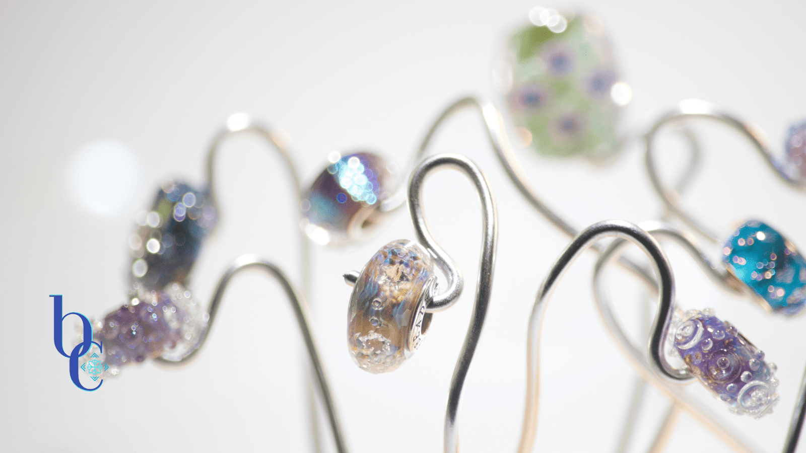 A macro image of an art glass bead called Light Beyond Time by Elfbeads captured in a minature photo studio set resembling an alien flower garden with silver wires suspending the beads over a pale grey backdrop.