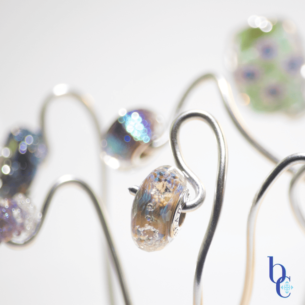 A macro image of an art glass bead called Light Beyond Time by Elfbeads captured in a minature photo studio set resembling an alien flower garden with silver wires suspending the beads over a pale grey backdrop.