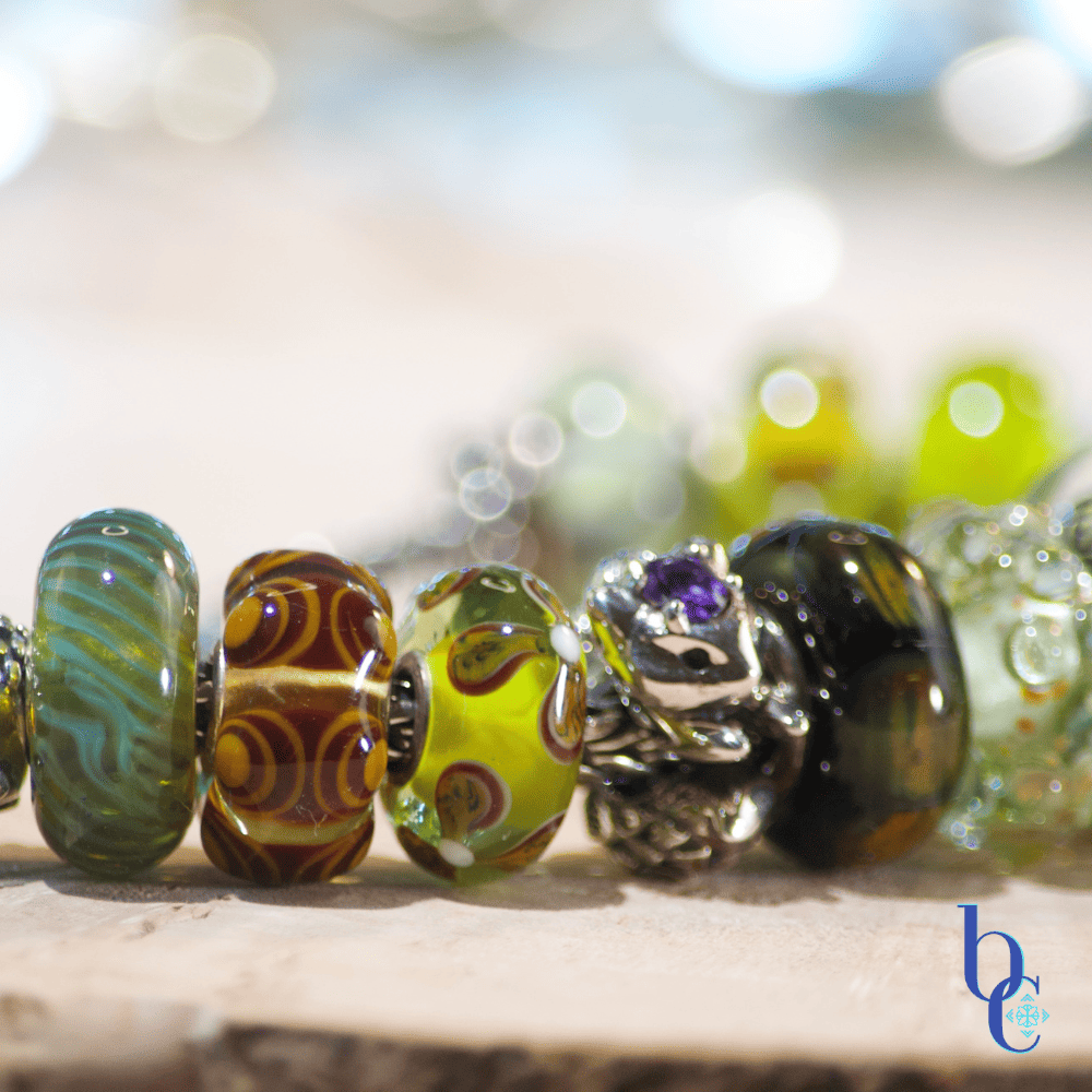 Macro detail of a silver fox charm with an amethyst gemstone accent, styled on a bracelet between green glass forest beads.