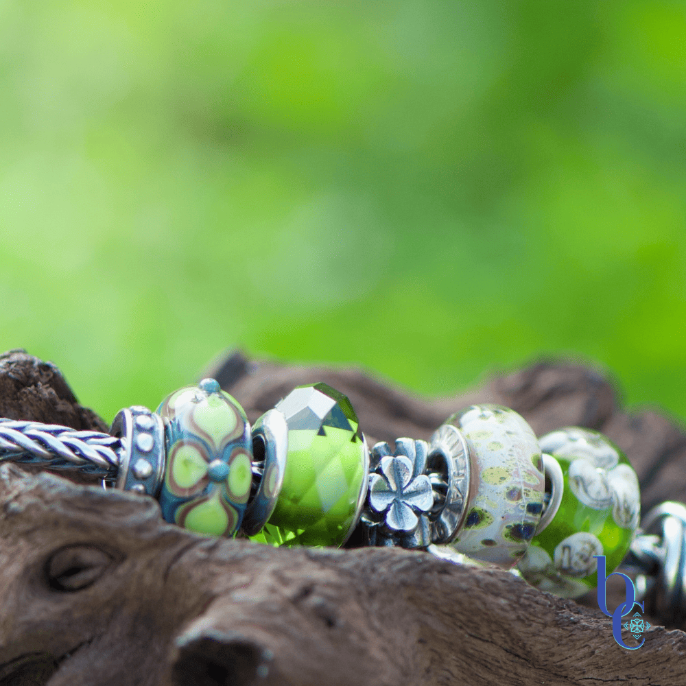A macro featuring the Elfbeads Turquoise Tripetual glass bead in the Bijoux Chat European bracelet design, Lucky Greens resting on rustic wood surrounded by green grass.
