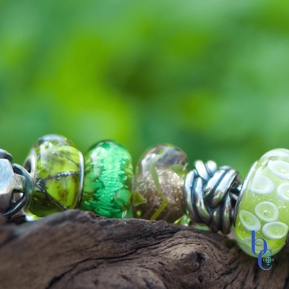 A macro featuring the Trollbeads Fortune Keeper and Trollbeads Earth glass beads in the Bijoux Chat European bracelet design, Lucky Greens resting on rustic wood surrounded by green grass.