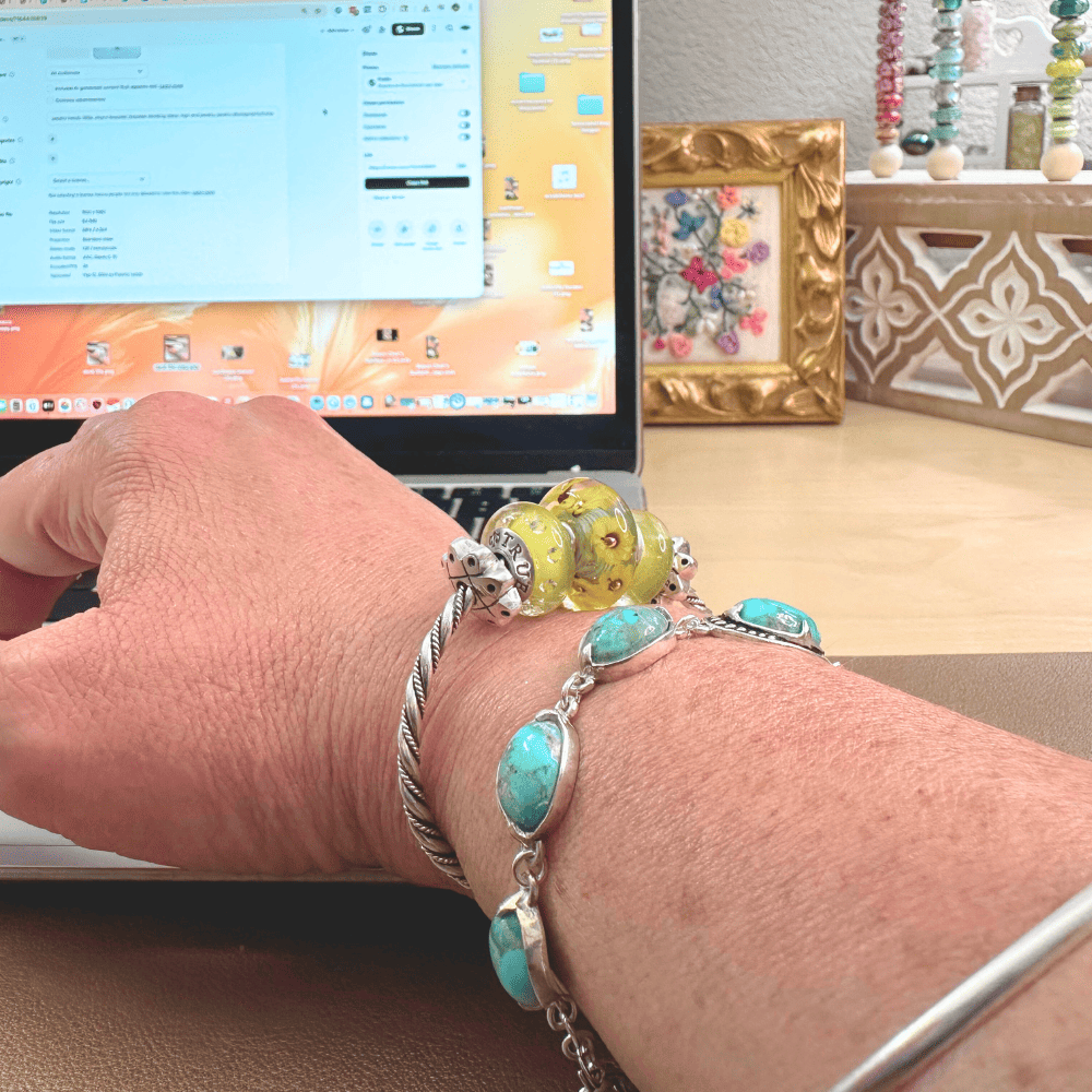 A close-up lifestyle shot of a wrist wearing a silver sunflower charm bangle, resting on a laptop keyboard. The bangle sits high on the wrist, demonstrating it doesn't interfere with typing.