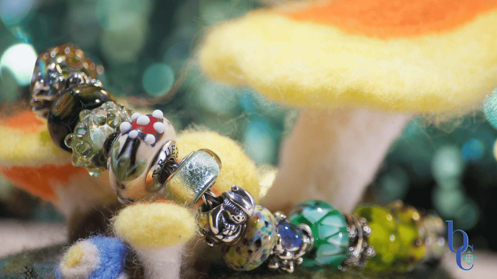 Bijoux Chat’s Fairytale Woodland European Charm Bracelet Design featuring Trollbeads, Moress, Truebeadz, Black Raven Beads and Pandora Pieces set on a piece of rustic wood with bokeh lighting in the background to simulate fireflies.