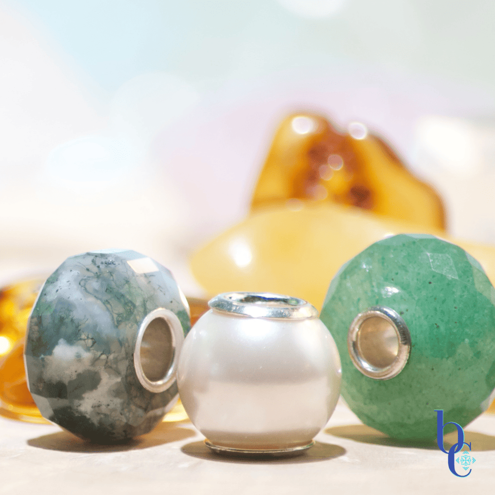 An Image of natural stone European bracelet beads with sterling silver cores. The lighting makes them sparkle and shine and shows their translucence and delicate nature. The pearl is especially featured in the image due to its delicate nature.