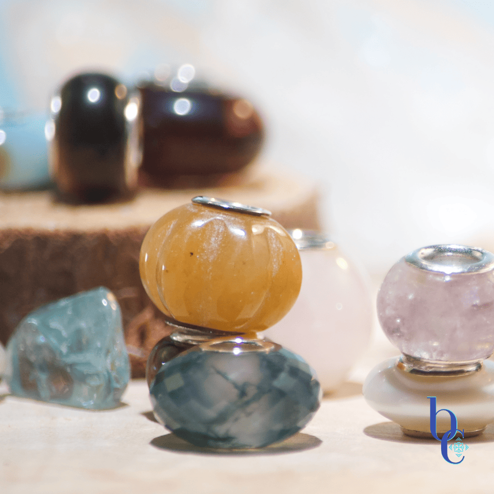 An Image of natural stone European bracelet beads with sterling silver cores. The lighting makes them sparkle and shine and shows their translucence and delicate nature. The carved yellow jade is especially featured in the image due to its delicate nature.