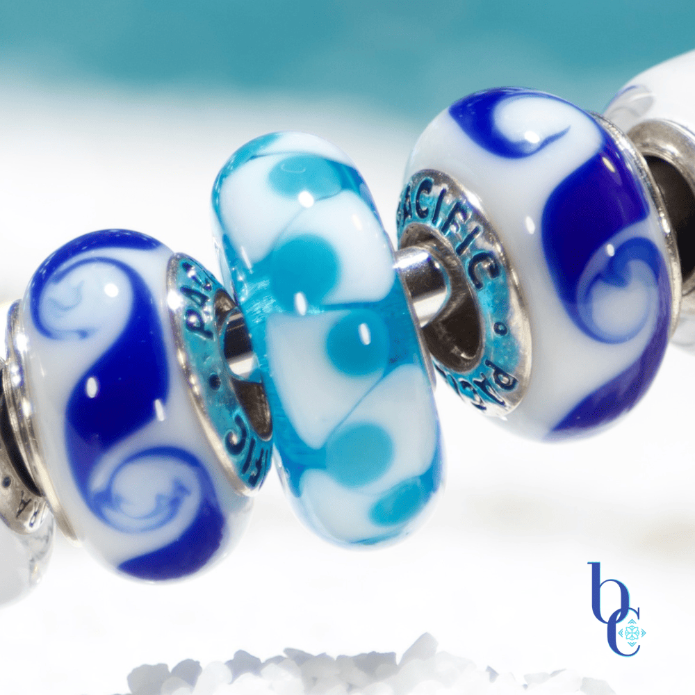 Bijoux chat's macro of a Trollbeads Blue Unique in our Blue Mediterranean Design featured on a white sand foreground with a blue sky backdrop behind.