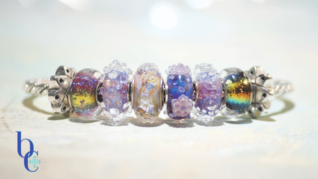 The image is of an ethereal blue bracelet design of glittering glass beads mixed with dichroic glass beads on a twisted sterling bangle.