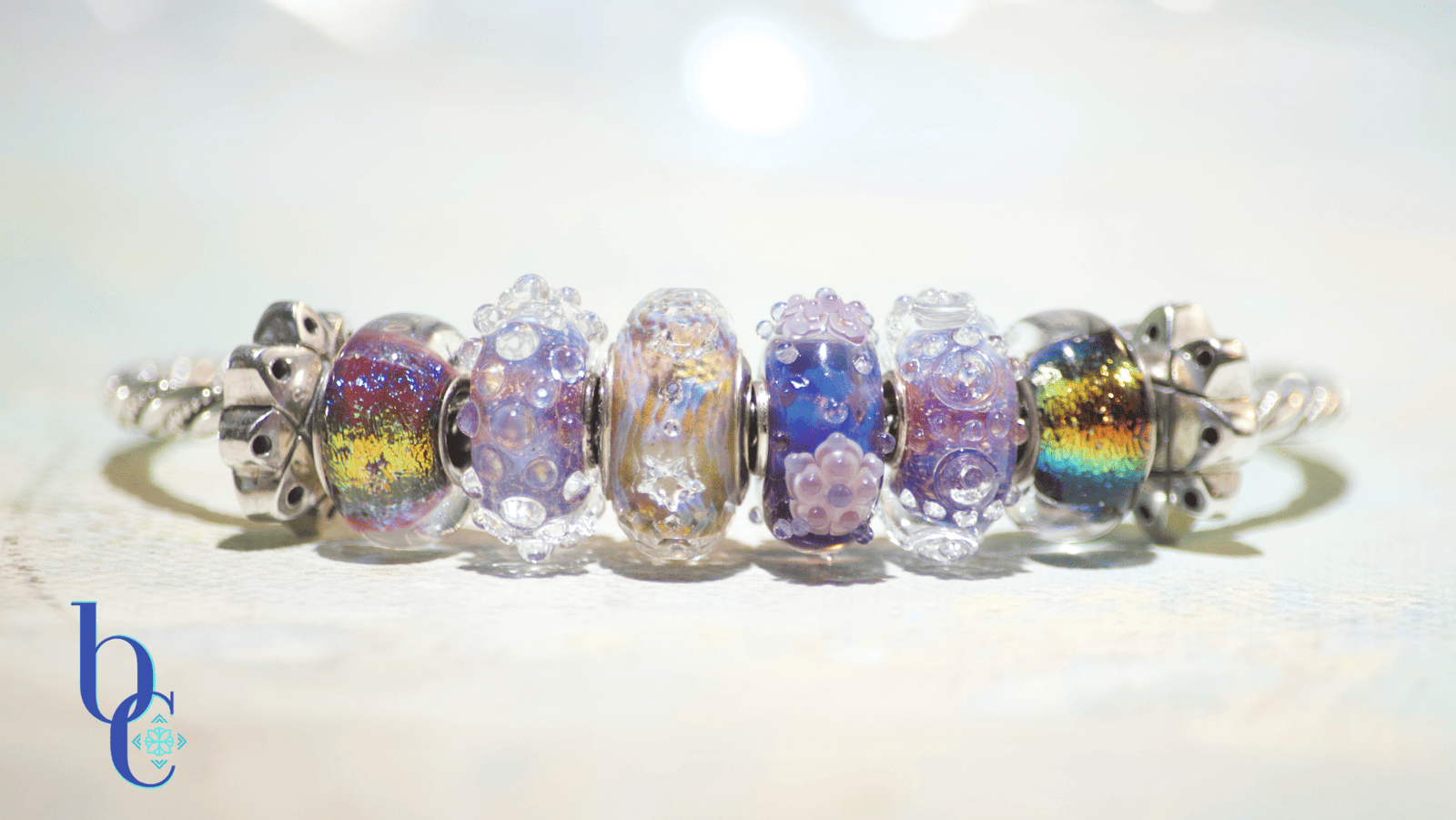 The image is of an ethereal blue bracelet design of glittering glass beads mixed with dichroic glass beads on a twisted sterling bangle.