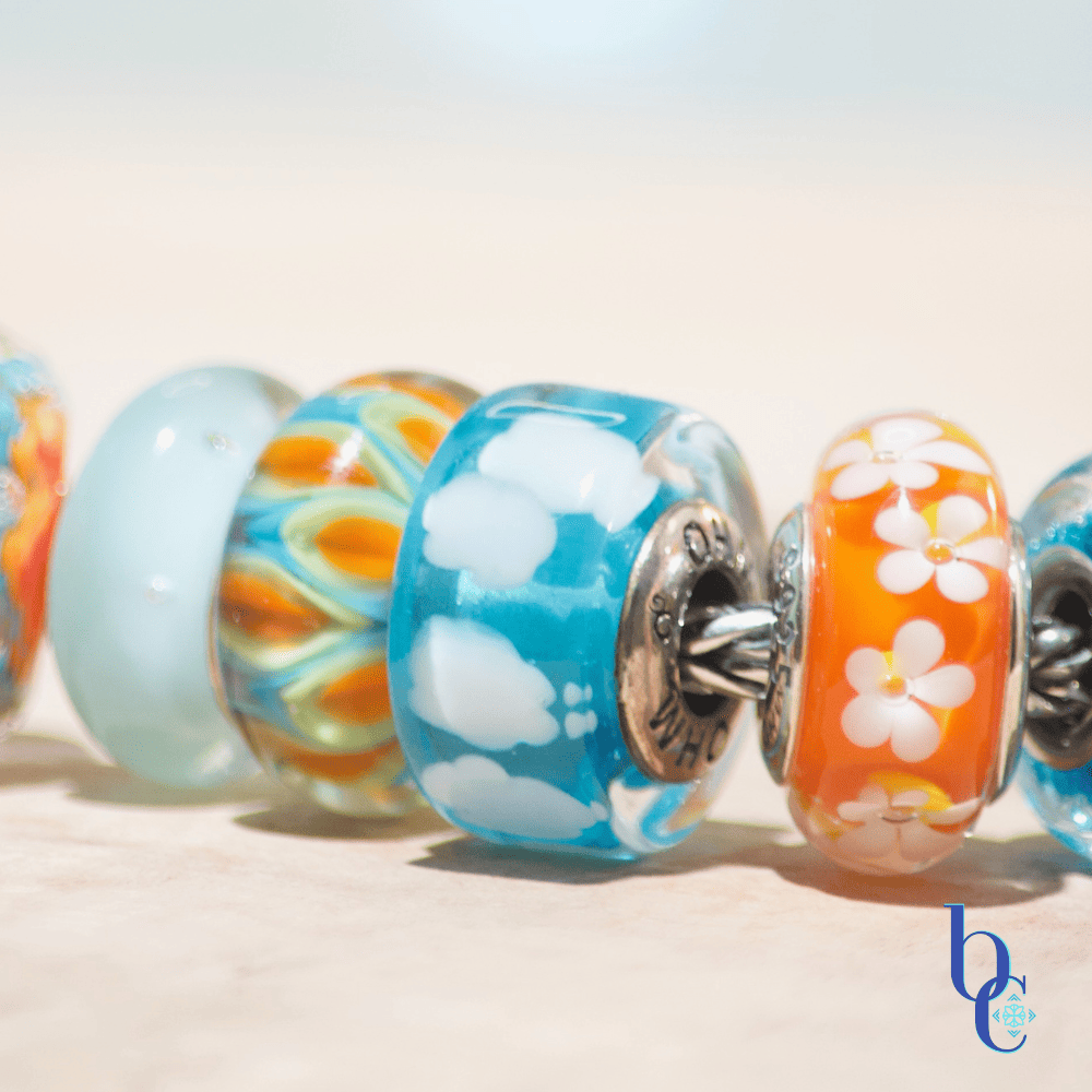 Banish the beige with our latest case study: Rhythm in Glass. Discover how to style a high-impact, complementary charm bracelet using bold cyan and tangerine artisan glass.