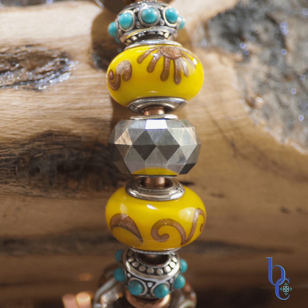 A macro image showing the featured beads of the Gilded Mesa design, an artisan 925 faceted golden pyrite bead, a Trollbeads leaf fall glass bead , a Black Raven Beads Maya First Sun and Maya Quiet Moon bead make the centerpiece of the bracelet design.
