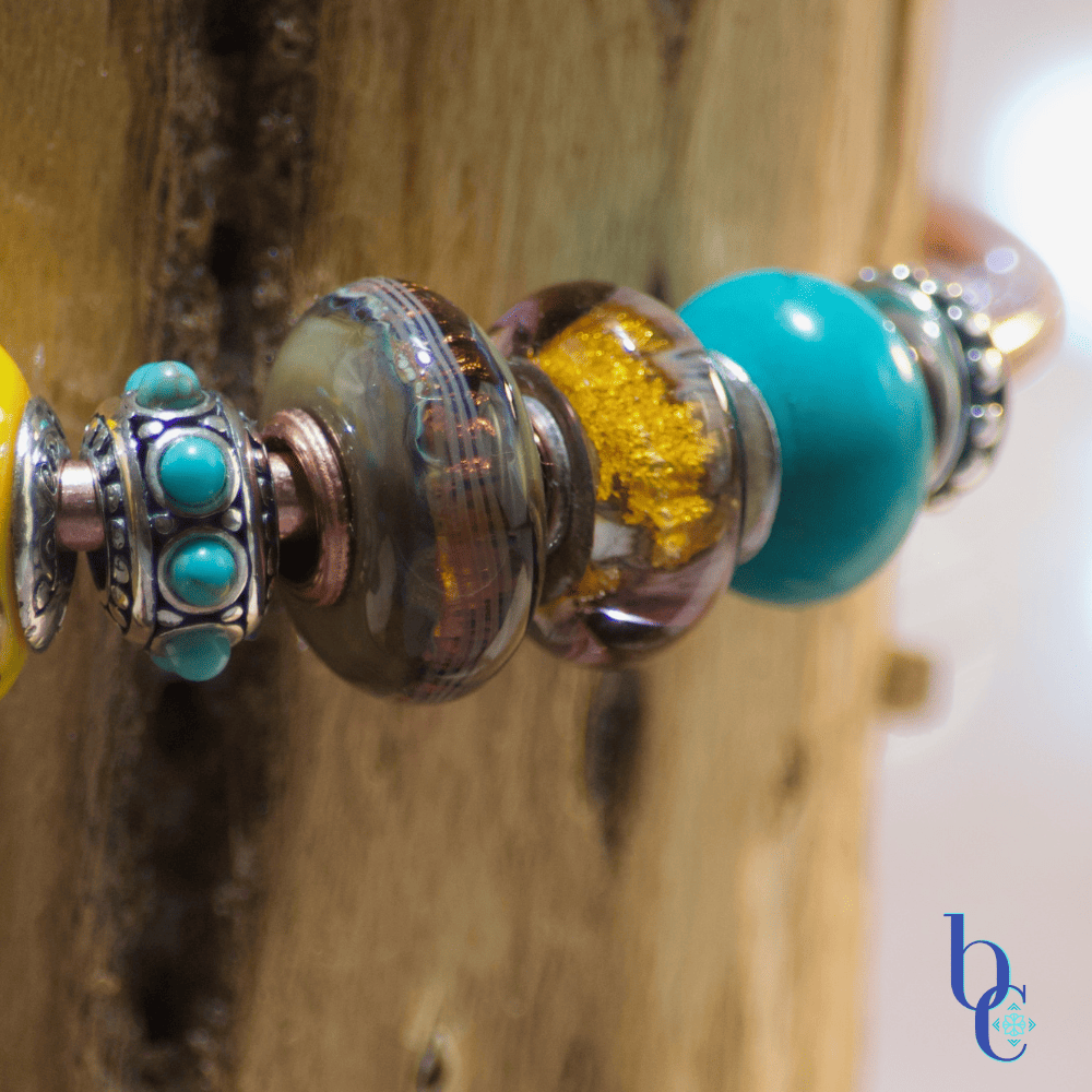 A macro image showing the featured beads of the Gilded Mesa design, a Kamane root threads glass bead, a Trollbeads leaf fall glass bead and a Redbalifrog turquoise bead.