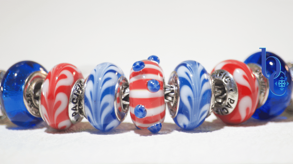 A minimalist flat lay of the Trollbeads Star Spangled bead flanked by deep red and true blue glass charms, resting on a stark, crisp white background.