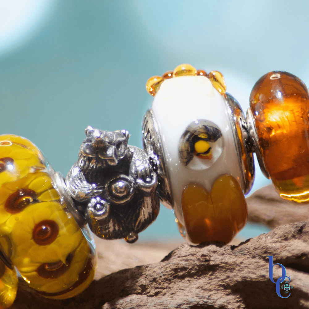 Extreme close-up of a European charm bracelet featuring a sculpted silver Black Raven honey bear charm nestled alongside translucent True Beadz honeybee glass bead.