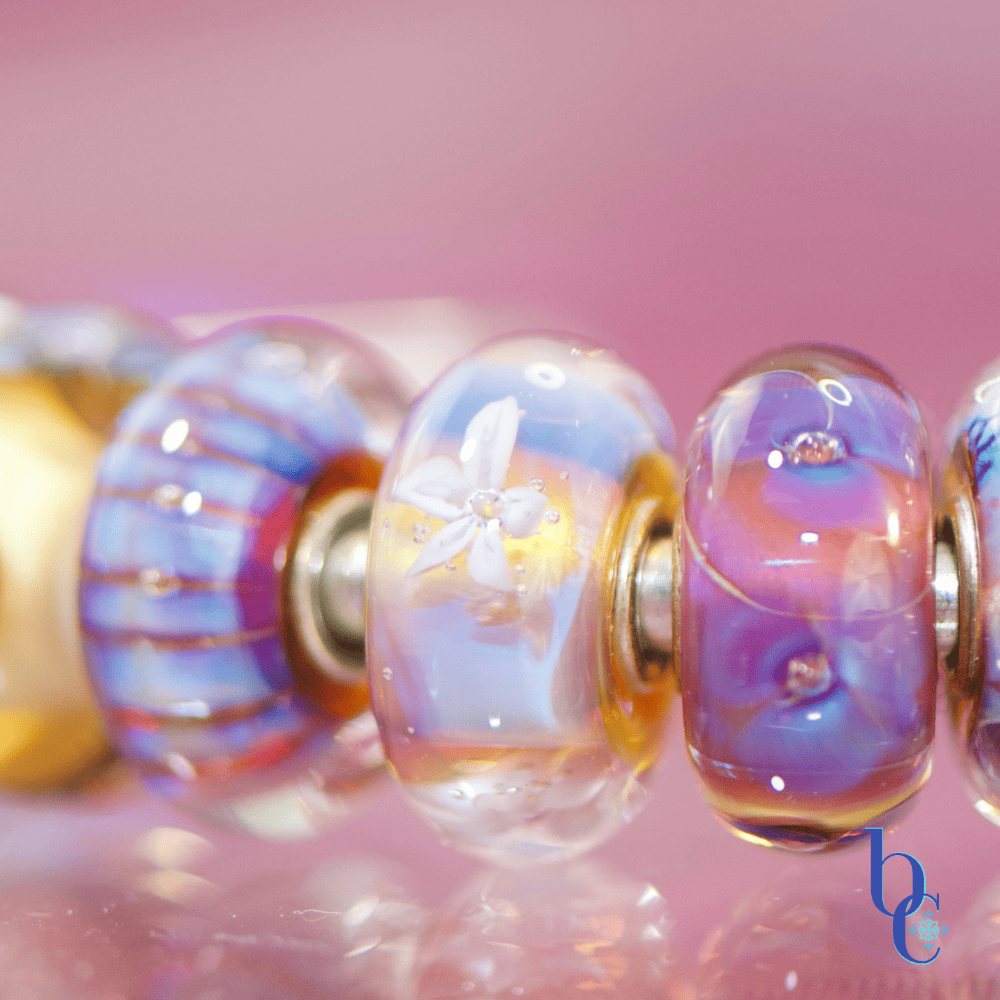 A macro studio shot of a vibrant purple and blue charm bracelet illuminated against a bokeh background, highlighting the details of retired artisan glass charms.
