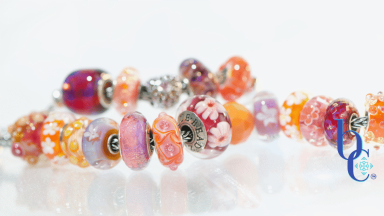 High-contrast macro photograph of a European-style charm bracelet featuring bright orange, hot pink, and purple artisan glass beads interspersed with highly textured silver floral charms, resting on an underlit plexi base.