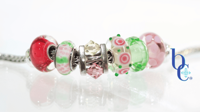 High-contrast macro photograph of a European-style charm bracelet featuring pink and green artisan glass beads interspersed with a rotating crystal charm, resting on an underlit plexi base.