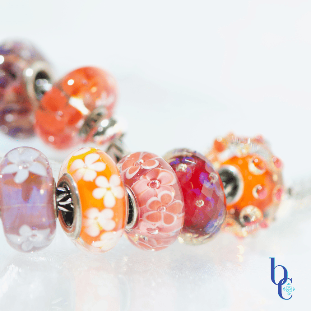 Extreme close-up of a single artisan glass bead showing an internal blend of hot pink and orange with subtle suspended glitter or flowers flanked by various beads in the design
