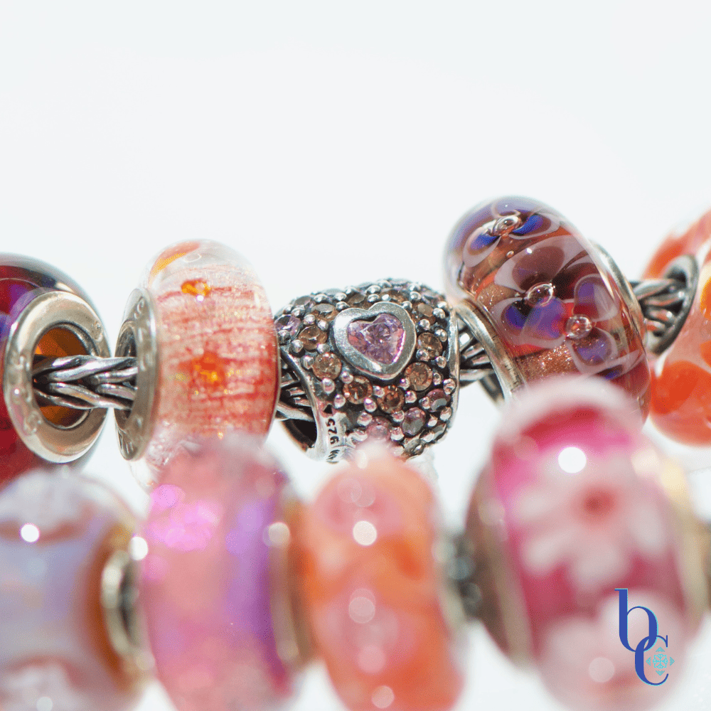 Extreme close-up of a single artisan glass bead showing an internal blend of hot pink and orange with subtle suspended glitter or flowers flanked by various beads in the design
