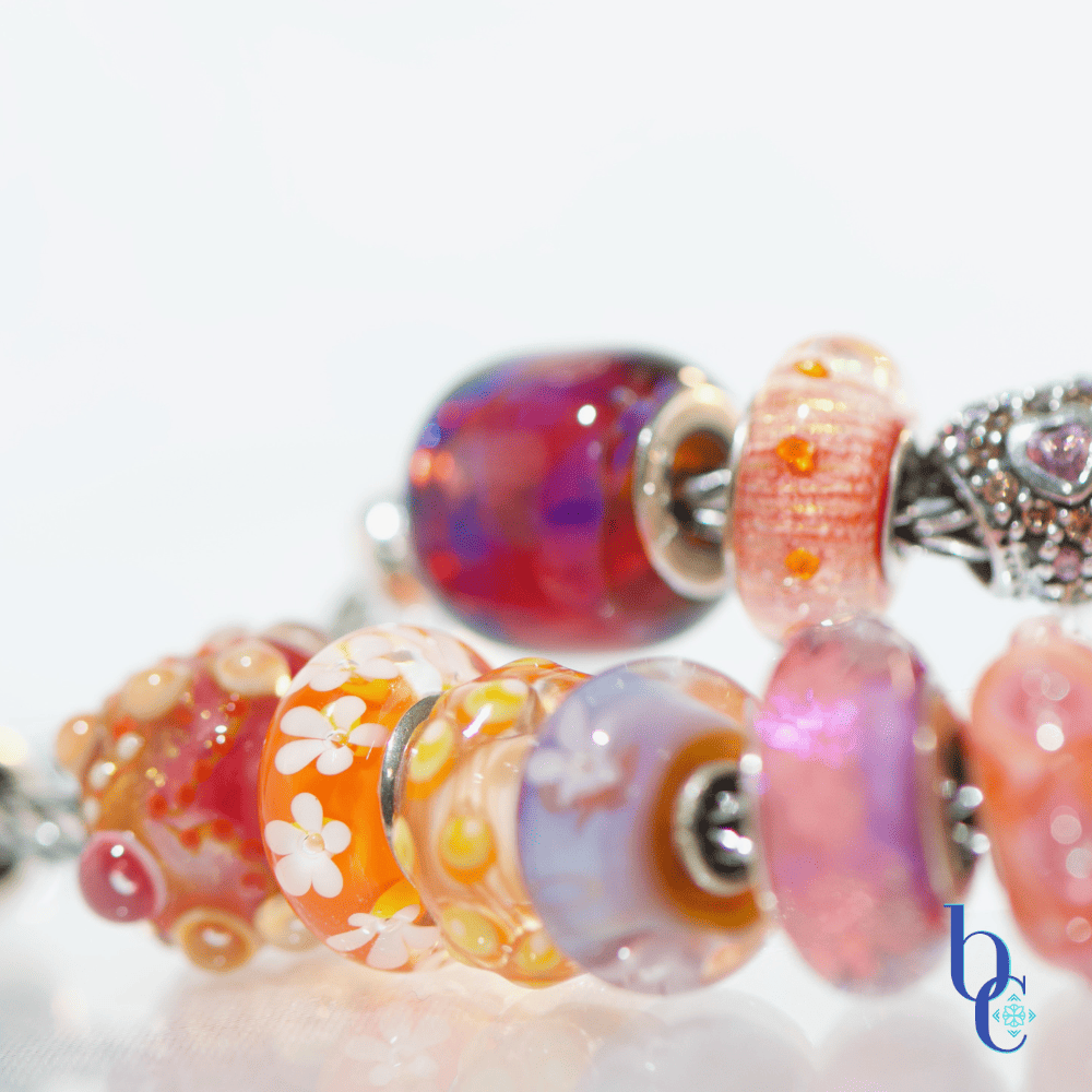 Extreme close-up of a single artisan glass bead showing an internal blend of hot pink and orange with subtle suspended glitter or flowers flanked by various beads in the design
