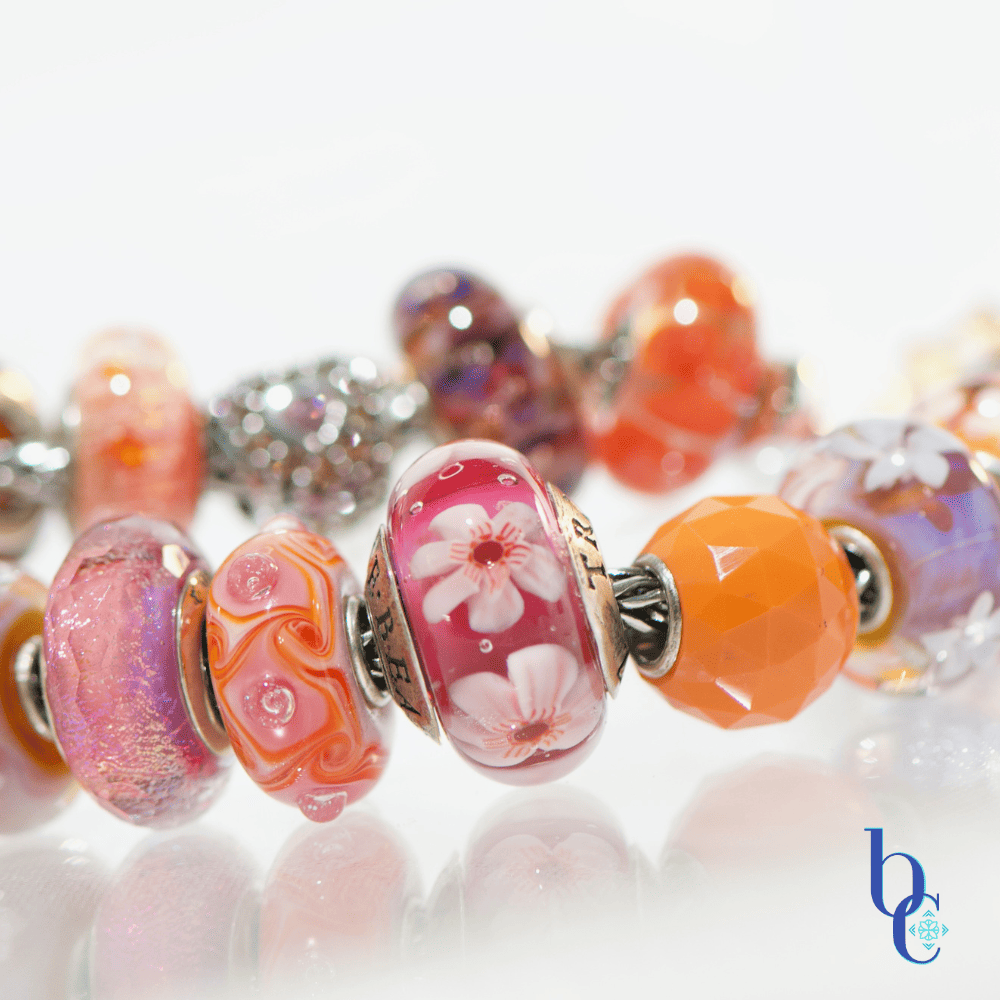 Extreme close-up of a single artisan glass bead showing an internal blend of hot pink and orange with subtle suspended glitter or flowers flanked by various beads in the design
