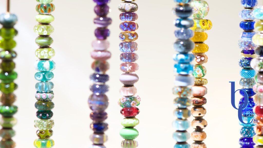 An image ofo hundreds of brightly colored glass European charm beads from my collection on a homemade rack in my studio set on a white backdrop.