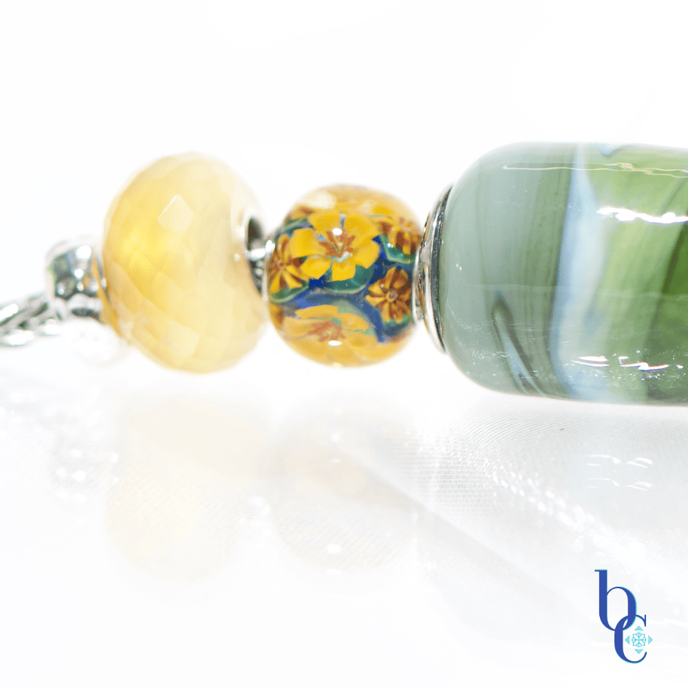 Explore "Ripples in Glass"—a 5-piece charm bracelet design inspired by Vermont summer lakeside life. Featuring TrueBeadz, Trollbeads, and natural faceted minerals styled for an artsy aesthetic on a white background.