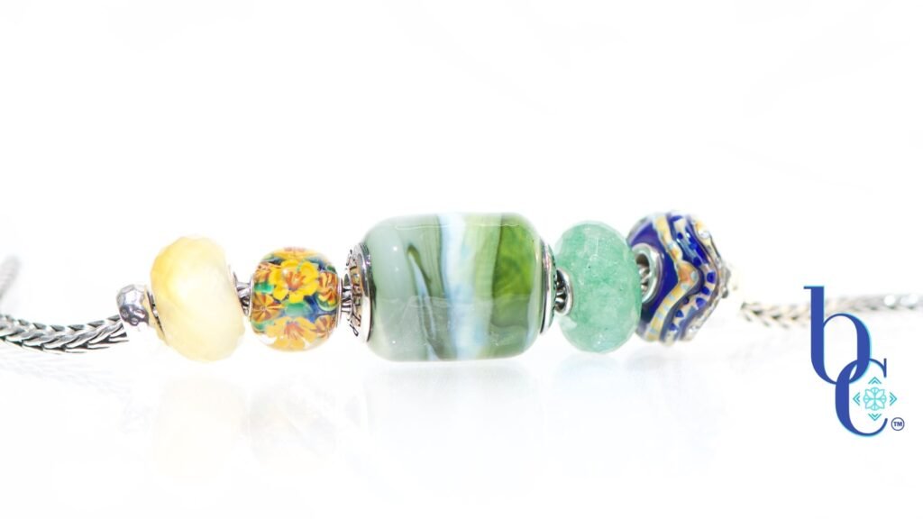 Explore "Ripples in Glass"—a 5-piece charm bracelet design inspired by Vermont summer lakeside life. Featuring TrueBeadz, Trollbeads, and natural faceted minerals styled for an artsy aesthetic on a white background.