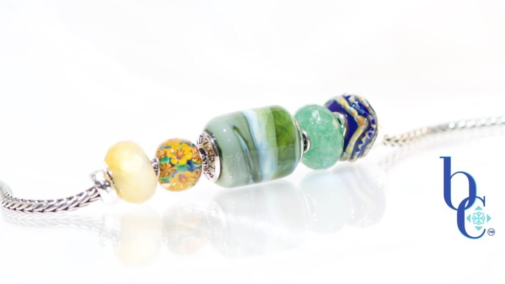Explore "Ripples in Glass"—a 5-piece charm bracelet design inspired by Vermont summer lakeside life. Featuring TrueBeadz, Trollbeads, and natural faceted minerals styled for an artsy aesthetic on a white background.